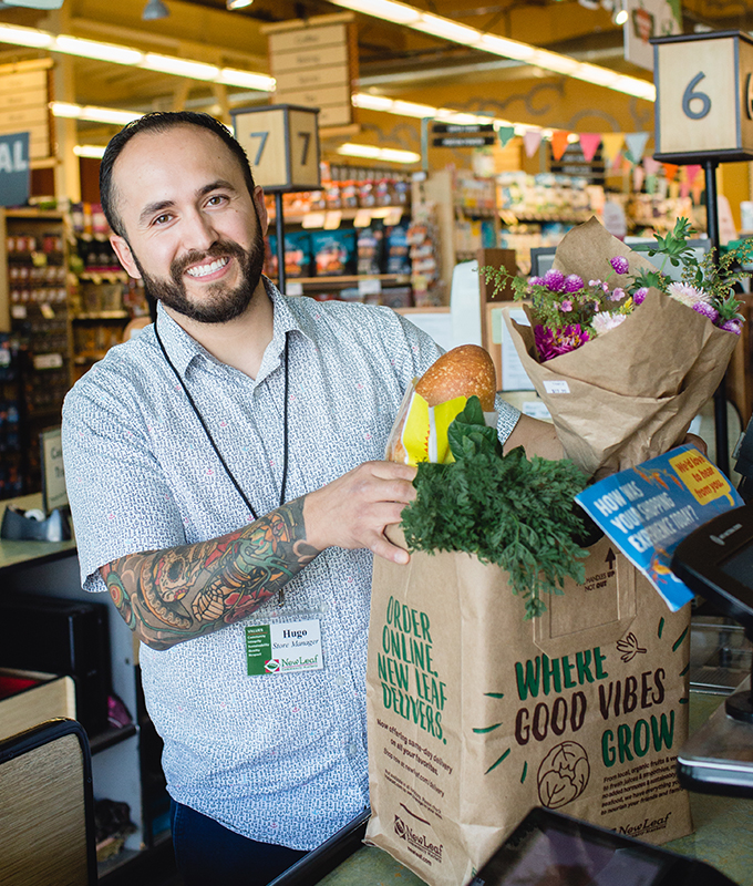 a new leaf employee smiling and holding a paper bag of groceries