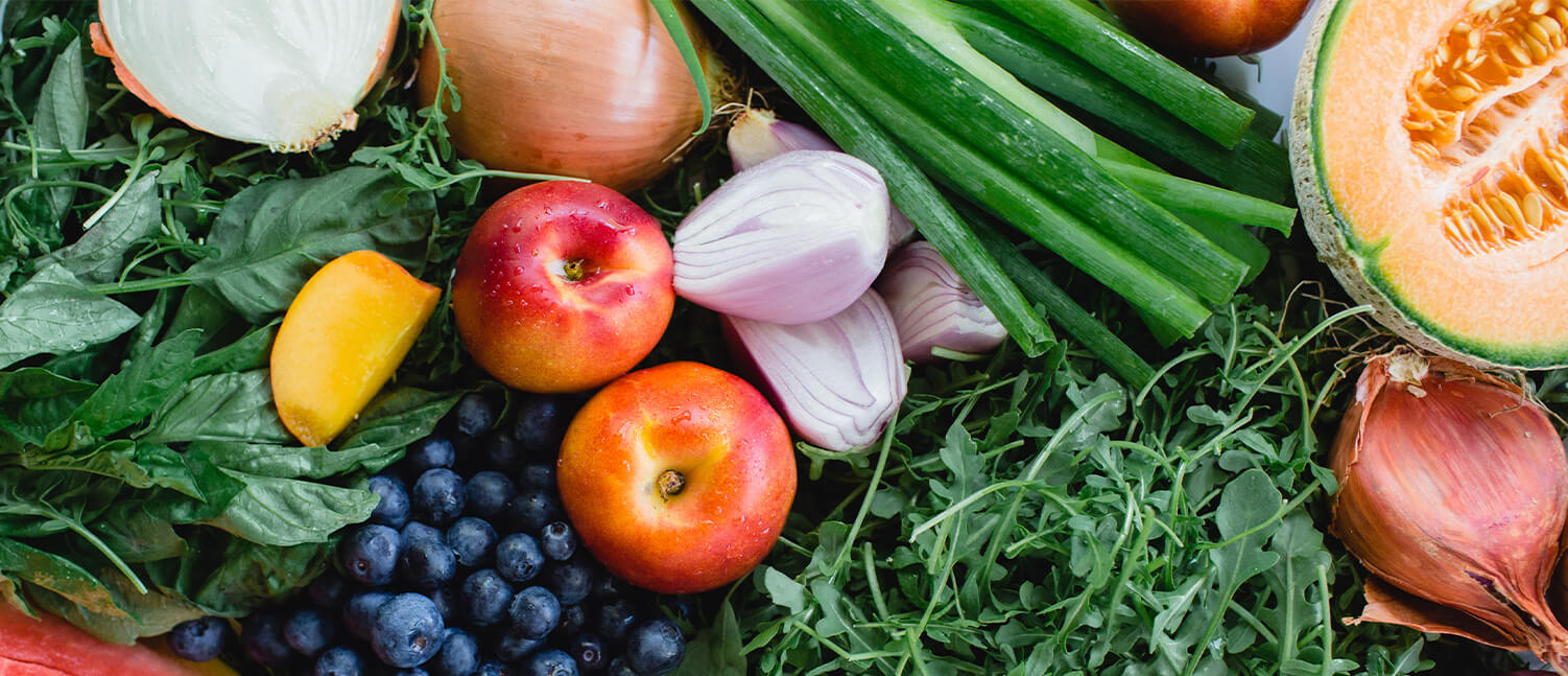 a variety of fresh fruite and vegetables  including green herbs, apples, blueberries, onion, melon and more.